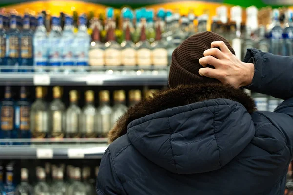 Yekaterinburg, russland - november 2019. ein mann in gedanken vor den reihen von alkohol in einem supermarkt. eine breite Palette alkoholischer Getränke. der Käufer wählt die Ware aus — Stockfoto