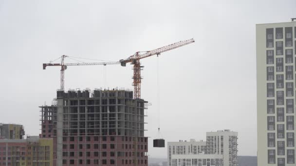 Ein Baukran hebt eine Last. Turmdrehkran auf einer Baustelle hebt eine Last am Hochhaus. der Prozess des Baus eines mehrstöckigen modernen Wohnhochhauses. — Stockvideo