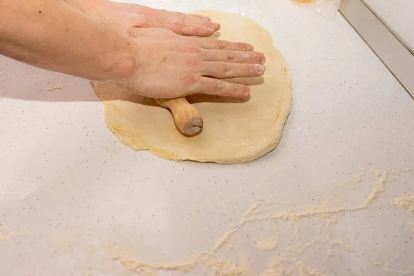 Saca la pasta. panadero lanza la masa en una mesa de cocina de madera espolvoreada con harina —  Fotos de Stock