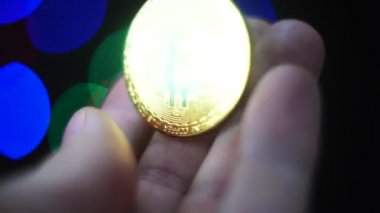 Altın parlayan bitcoin palmiye arka planında döner. Zengin olma arzusu. Titreyen bir el altın para almak ister. Seçici odak