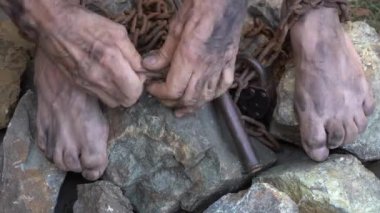 Köle işçilik sahnesi. Bir kölenin elleri ve ayakları demir zincirlerle bağlıdır. Kölelikten kurtulma girişimi. Zincirleri kır.