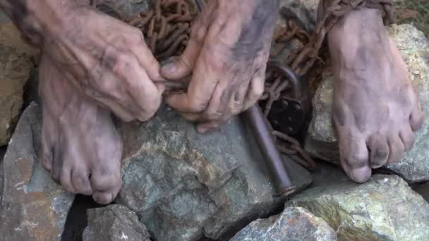 A cena do trabalho escravo. As mãos e os pés de um escravo estão amarrados com correntes de ferro. Uma tentativa de libertar-se da escravatura. Quebre as correntes . — Vídeo de Stock