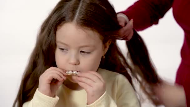 一个六岁的小女孩用发夹玩 妈妈用辫子编辫子 妈妈给一个长头发的女儿编辫子 在白色背景上分开 — 图库视频影像