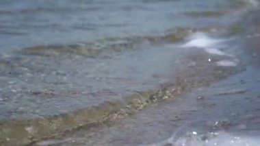 Pebbles in shallow water. Clean lake in the sunlight in the afternoon. Close-up. Waves are floating along the lake