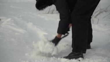 A man removes snow from a forest road to drive a car. Swing the snow back with a small folding spade.
