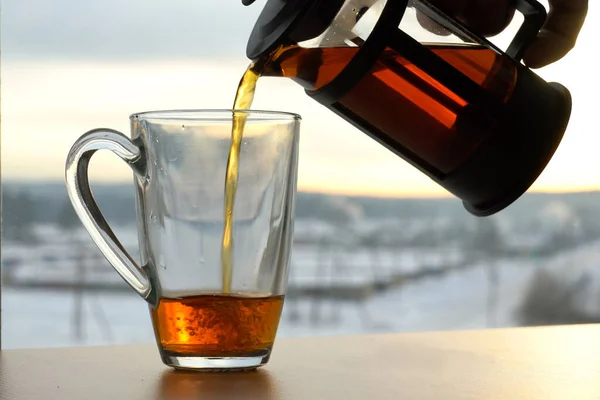 Nalijte ranní čaj. Kotlík nalévá černý čaj do šálku v ranním slunci na okno — Stock fotografie