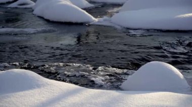 Gün batımında bir ormanda, beyaz karların arasında hızlı bir nehir..