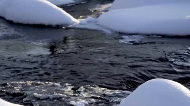 Gün batımında bir ormanda, beyaz karların arasında hızlı bir nehir..