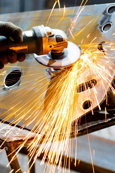 Elle öğütücü kullanarak metal ürünü işliyor. Öğütücü kullanan bir işçi metali keser..