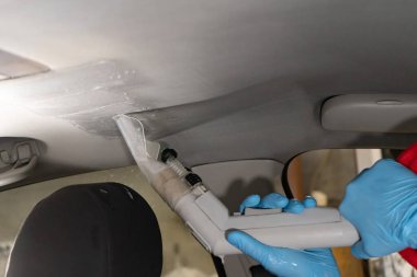 Arabanın kuru temizlemesi. İşçi dezenfekte etmek için elektrikli süpürge kullanıyor..