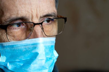 Gözlüklü ve tıbbi maskeli yaşlı bir adamın portresi..