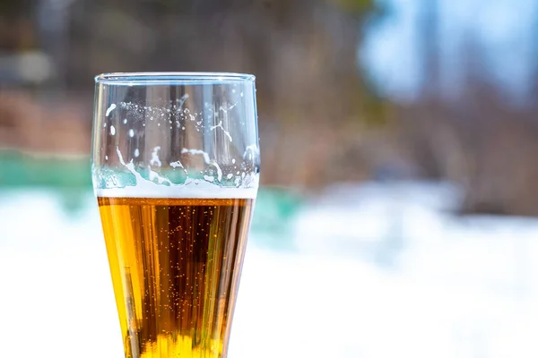 Light beer in a glass goblet on a picnic with snow background. Beer foam on the walls of a glass in the sunlight.