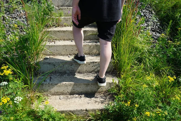 Legs of a man climbing the stairs among the grass in the summer on a sunny day. The calf muscles.