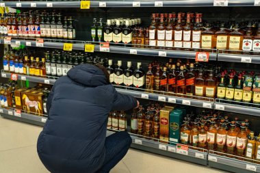 Yekaterinburg, Rusya - Kasım 2019. Süpermarkette içki sıralarının önünde düşüncelere dalmış bir adam. Çok çeşitli alkollü içecekler. Malları alıcı seçer..