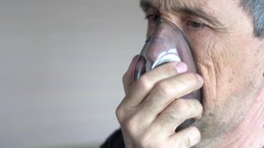 Bir adam maske kullanarak oksijen soluyor. Yaşlı bir adamın soluk alıp verişini yakından çek..