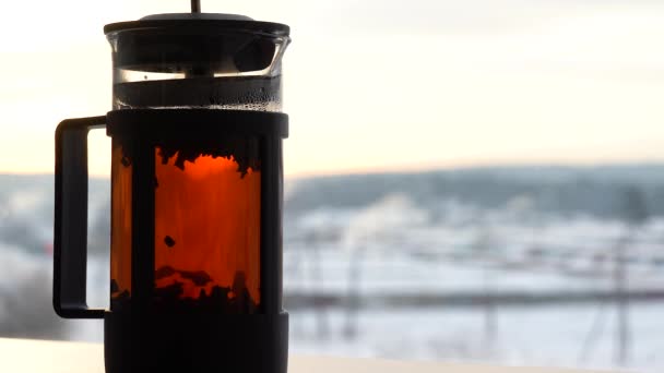 红茶颗粒漂浮在玻璃杯茶壶中 酿制而成 窗户上的水壶里放着红茶 冬天的早晨外面的窗户上可以看到雪 在冬日的早晨 — 图库视频影像