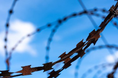 Mavi gökyüzünün arka planında paslı dikenli tel var. Mavi gökyüzü ve beyaz bulutların üzerinde dikenli tellerin silueti.