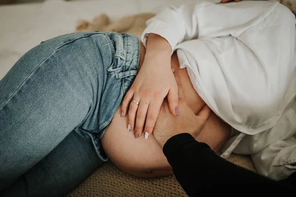 Feliz joven marido besando a su esposa embarazada sonriente y abrazando el bulto del vientre en la cama blanca . —  Fotos de Stock