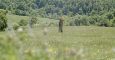 Genç bir kadın çimenlerin arasında ağır çekimde yürüyor.