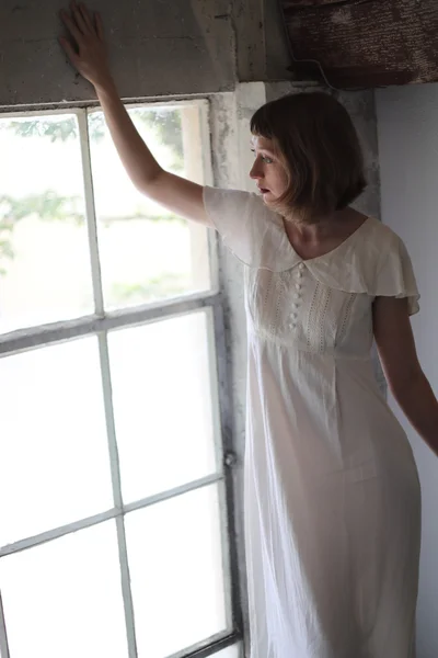 Vacker kvinna i en vit klänning i fönster ljus — Stockfoto
