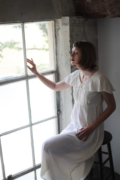 Belle femme dans une robe blanche dans la lumière de la fenêtre — Photo