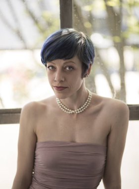 Güzel mavi gözlü, mavi saçlı çok çekici bir kadının fotoğrafı. Doğruca kameraya bakıyor ve leylak rengi güzel bir elbise giyiyor..