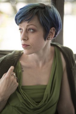 Güzel mavi gözleri ve mavi saç çok çekici bir kadın fotoğrafı. O uzakta kameradan arıyor ve bir güzel yeşil üst giyiyor.