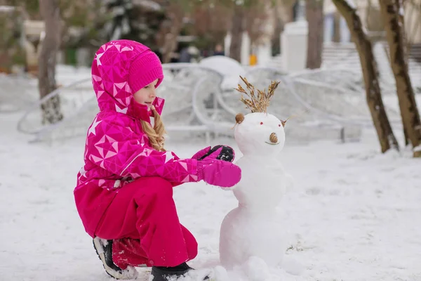 Ευτυχισμένο παιδί κορίτσι παίζει με έναν χιονάνθρωπο — Φωτογραφία Αρχείου