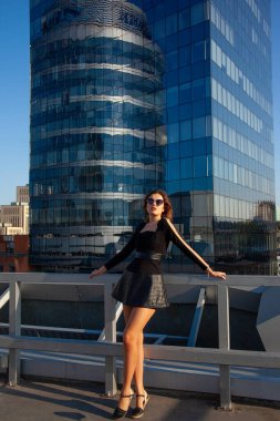 Genç anlamlı kadın mavi gökdelenlerin arka planında duruyor. Şehir modası konsepti, yumuşak odak