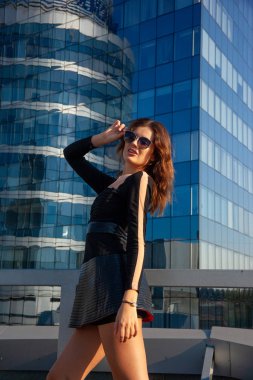 Genç anlamlı kadın mavi gökdelenlerin arka planında duruyor. Şehir modası konsepti, yumuşak odak