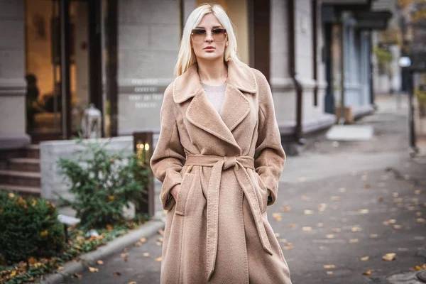 Young beautiful blond woman in an autumn coat stands on a city street. Soft focus. Fashionable concept. — Stock Photo, Image