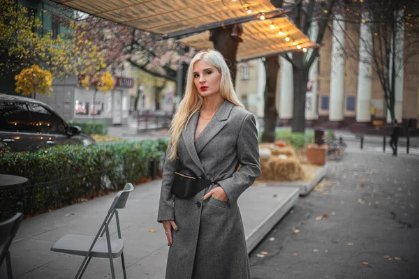 Mulher loira bonita nova em um casaco de outono está em uma rua de cidade. Foco suave. Conceito na moda . — Fotografia de Stock
