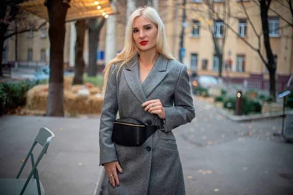 Mulher loira bonita nova em um casaco de outono está em uma rua de cidade. Foco suave. Conceito na moda . — Fotografia de Stock