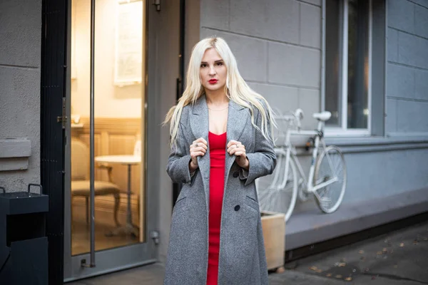 Mulher loira bonita nova em um casaco de outono está em uma rua de cidade. Foco suave. Conceito na moda . — Fotografia de Stock