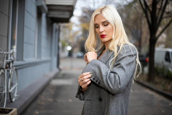 Mulher loira bonita nova em um casaco de outono está em uma rua de cidade. Foco suave. Conceito na moda . — Fotografia de Stock