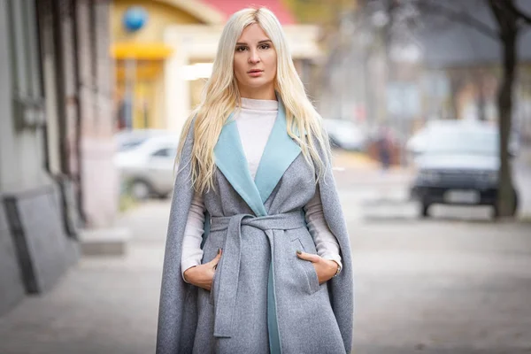 Mulher loira bonita nova em um casaco de outono está em uma rua de cidade. Foco suave. Conceito na moda . — Fotografia de Stock