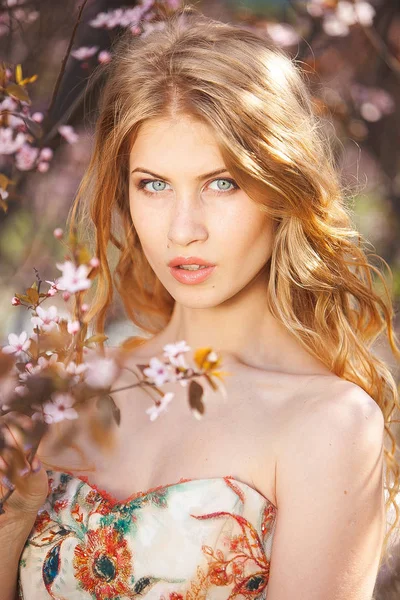 Модна зовнішня фотографія красивої чуттєвої жінки з довгим волоссям в розкішній сукні-шпинаті, що позує у весняному квітковому саду — стокове фото
