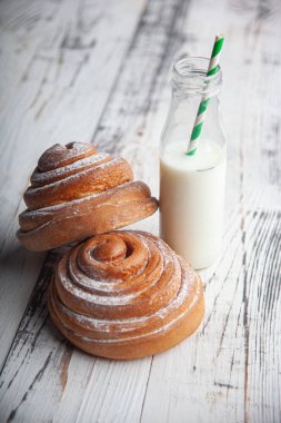 Tahta kesim masasında taze ev yapımı tarçın ruloları ve cam şişede süt.