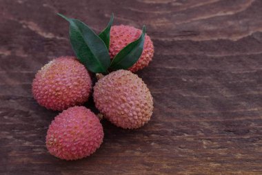 Kahverengi ahşap arka planda yeşil yapraklı kırmızı lychee üzümleri.