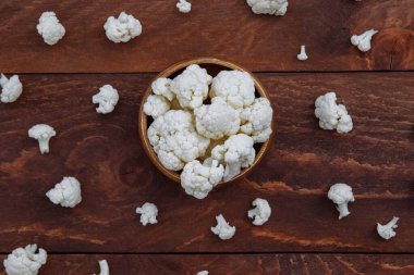 Beyaz karnabahar çiçekleri ahşap bir kasede yatar ve kahverengi ahşap bir masanın üstüne saçılırlar.