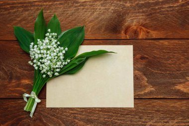 Yeşil yapraklı bir buket beyaz zambak ve kahverengi ahşap arka plan manzaralı yazı için yeri olan kağıt boş bir kart.