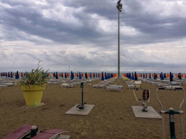 Bulutlu havalarda katlanmış ve uzanmış şemsiyelerle boş kumlu bir sahil manzarası