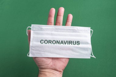 Adamın eli cerrahi maske tutuyor.