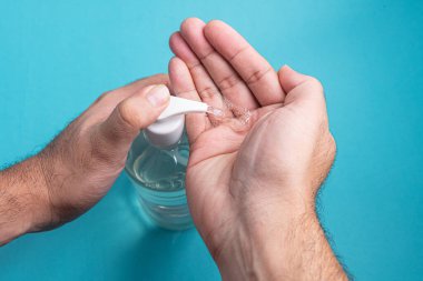 Açık mavi arka planda alkol jeli olan bir adam el ele veriyor.