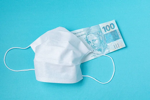 Surgical mask and brazilian real money, on the light blue background