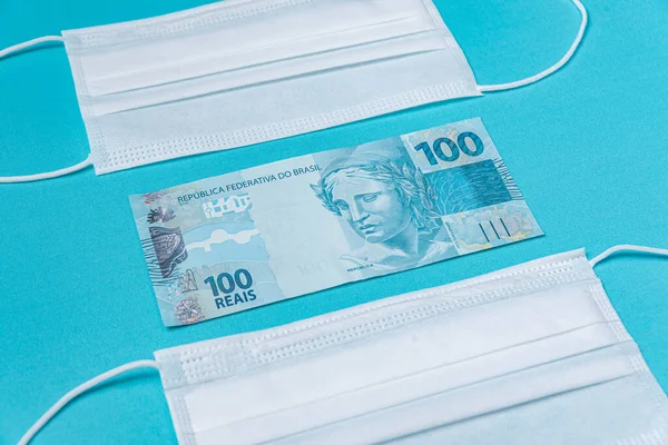Surgical mask and brazilian real money, on the light blue background