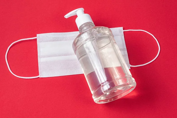 Container with alcohol gel and surgical mask on the red background