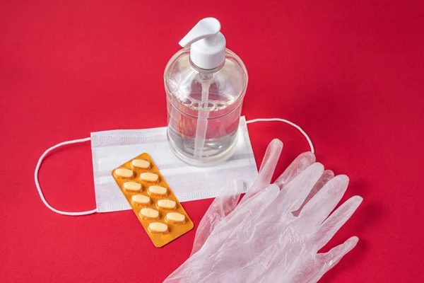 Alcohol gel container, surgical mask, medicine and gloves on the red background