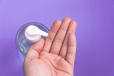 Açık mavi arka planda alkol jeli olan bir adam el ele veriyor.