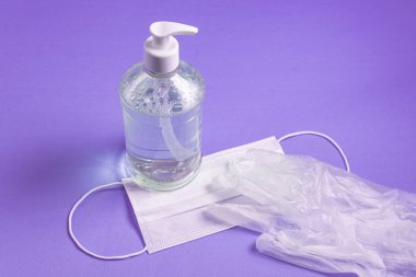 Açık mavi arka planda alkol jeli, eldiven ve cerrahi maske olan bir kap.